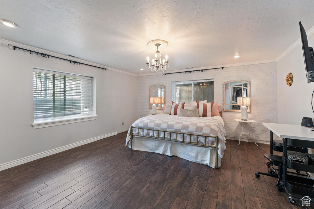 Bedroom featuring crown molding, an inviting chandelier, brick wall, dark wood finished floors, and baseboards