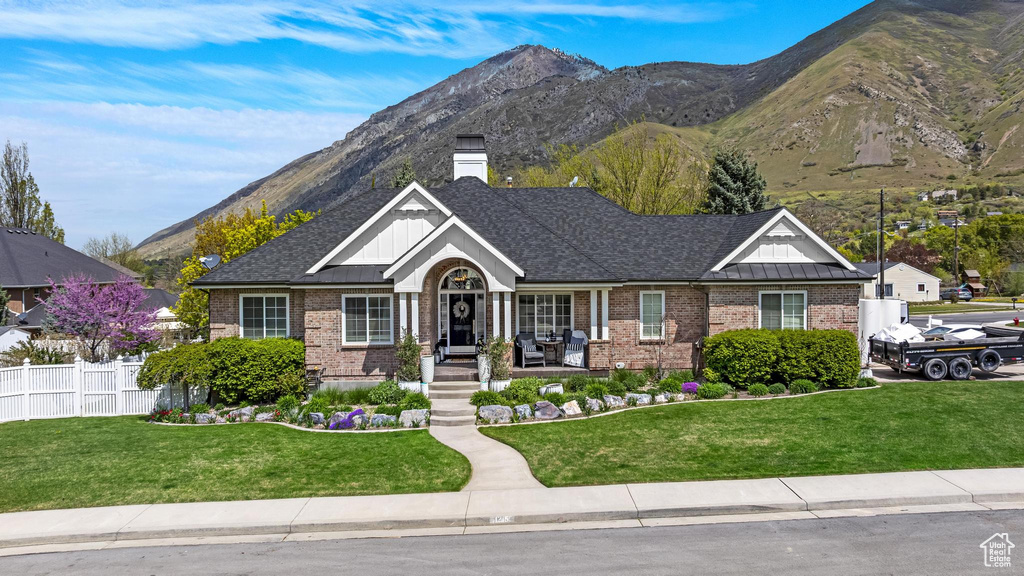 View of front of property with fence, a front yard, brick siding, board and batten siding, and a mountain view