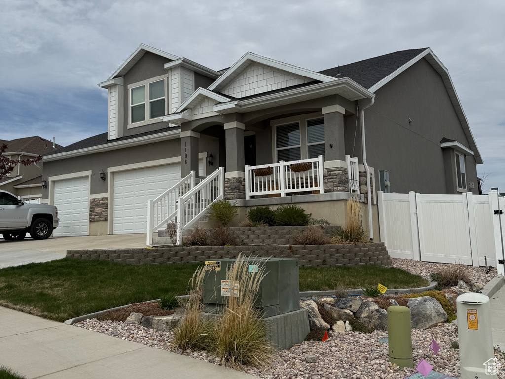 View of front of property with fence, covered porch, stone siding, an attached garage, and driveway