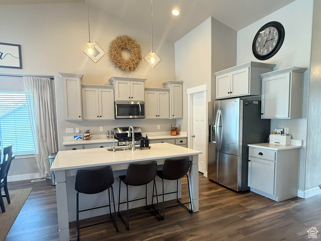 Kitchen featuring high vaulted ceiling, appliances with stainless steel finishes, baseboards, and a kitchen bar