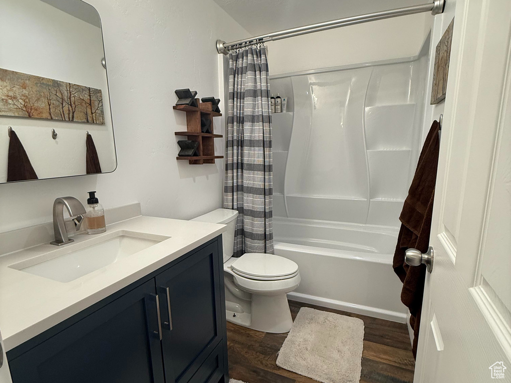 Full bath with a textured ceiling, wood finished floors, vanity, toilet, and shower / bathtub combination with curtain