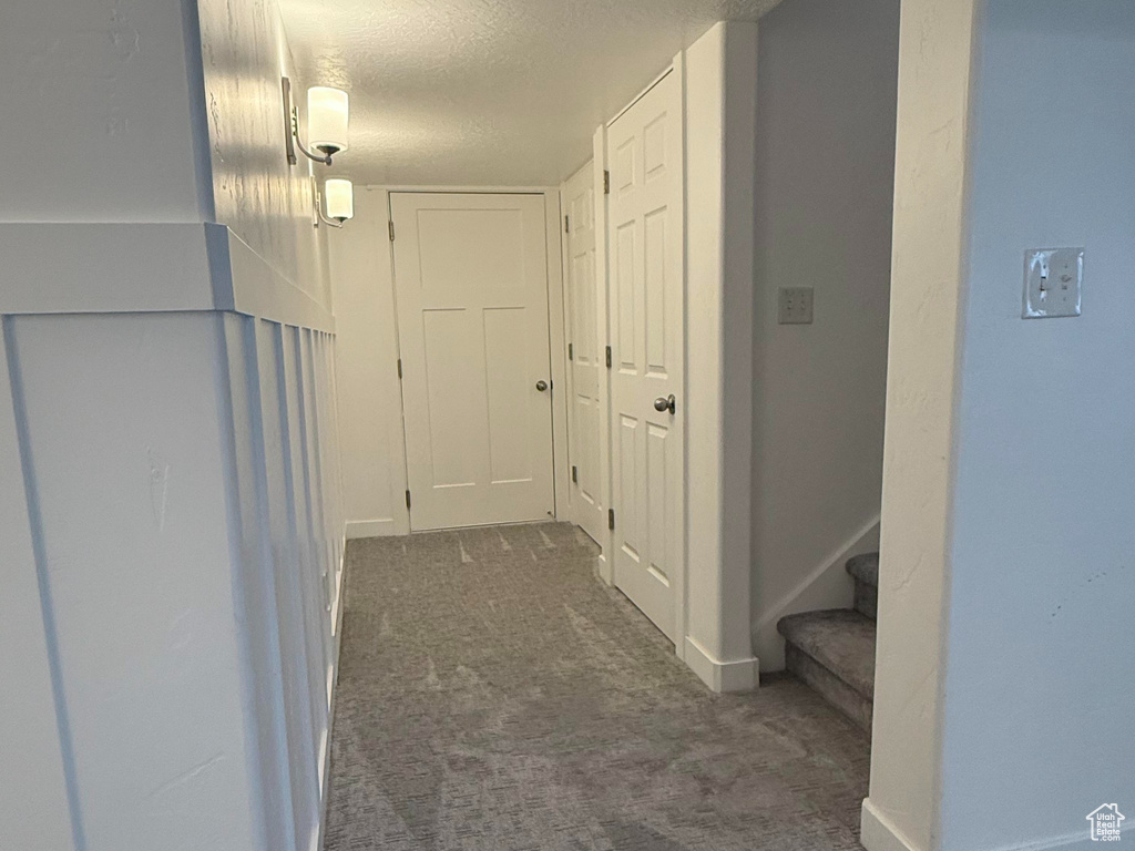 Hallway with stairs, a textured ceiling, baseboards, and carpet