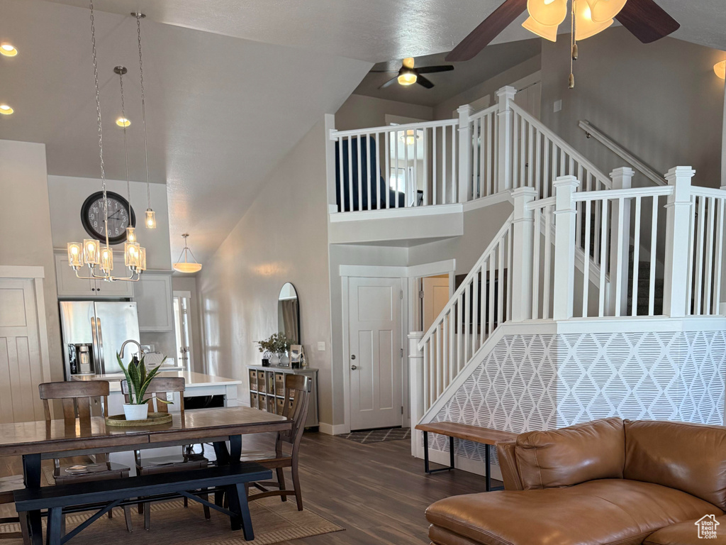 Living area featuring high vaulted ceiling, ceiling fan with notable chandelier, stairs, and wood finished floors