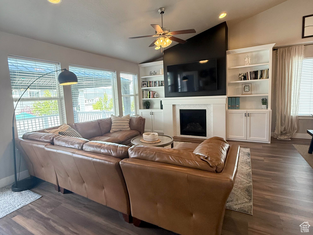 Living room featuring ceiling fan, a fireplace, vaulted ceiling, baseboards, and dark wood-type flooring