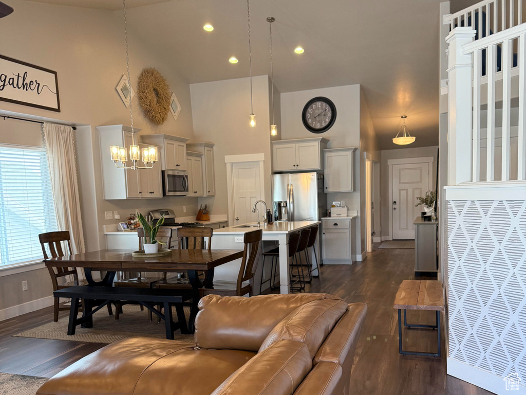 Living area featuring high vaulted ceiling, dark wood-style floors, baseboards, and ceiling fan with notable chandelier