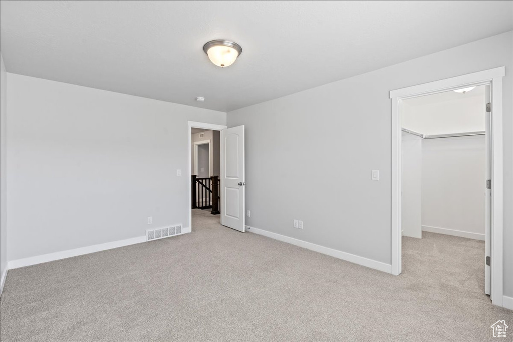 Unfurnished bedroom with light colored carpet, a walk in closet, baseboards, visible vents, and a closet
