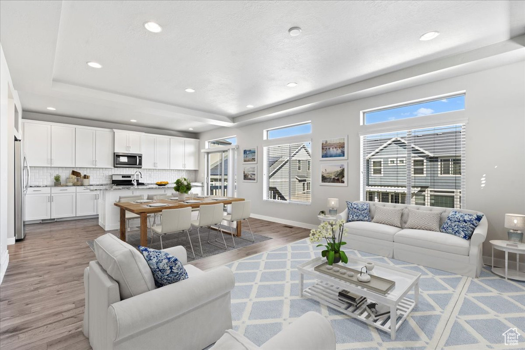 Living room with light wood-style flooring, a raised ceiling, baseboards, and recessed lighting