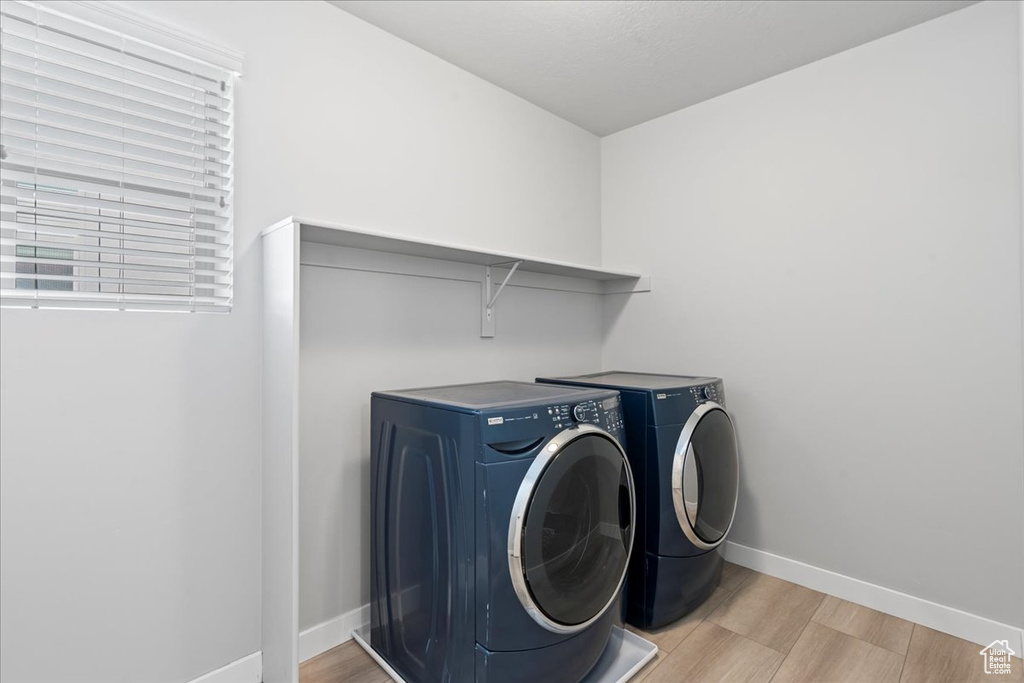 Clothes washing area featuring laundry area, light wood-style flooring, baseboards, and washing machine and dryer