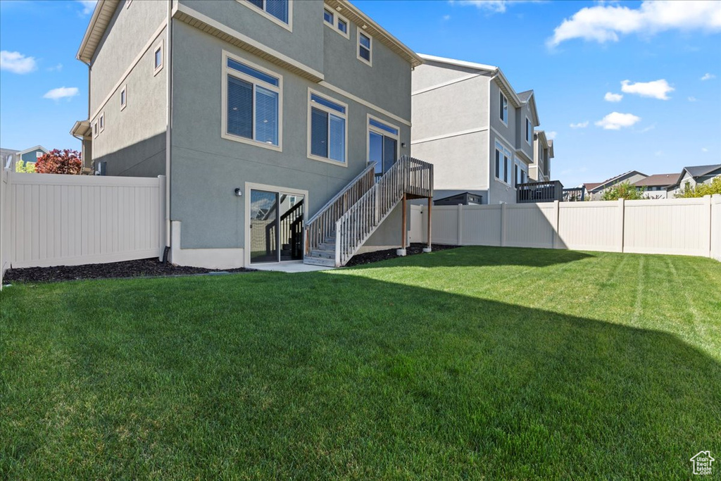 Back of property with stairs, a fenced backyard, stucco siding, and a yard