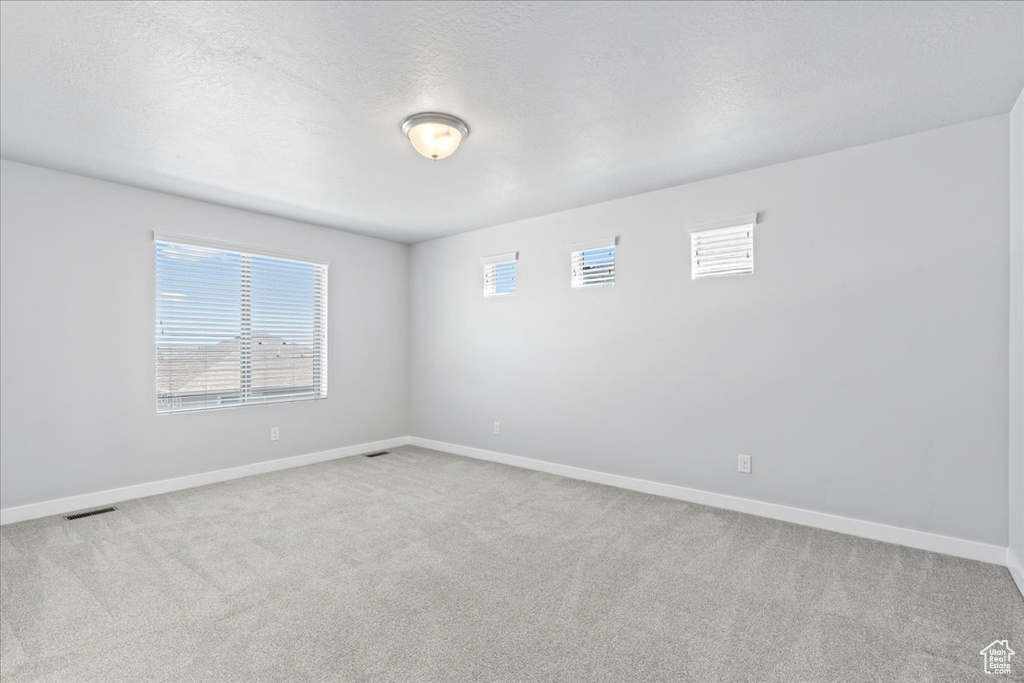 Carpeted spare room with a textured ceiling, baseboards, and visible vents