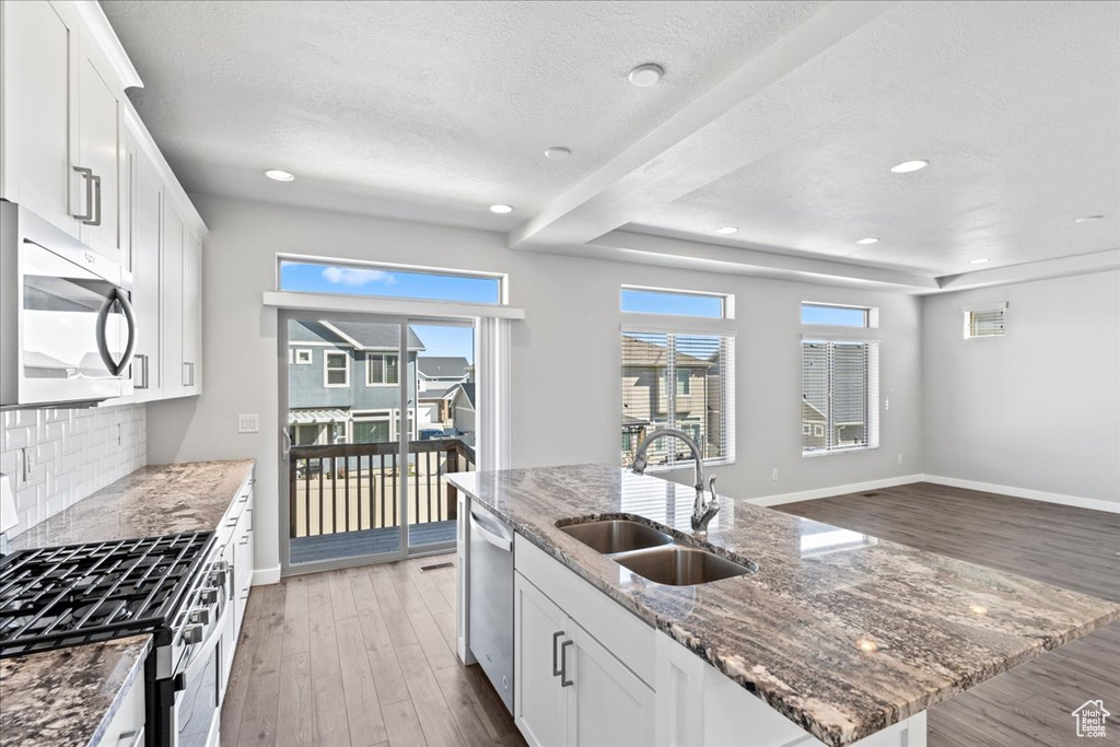 Kitchen with appliances with stainless steel finishes, a sink, a textured ceiling, light wood-style flooring, and tasteful backsplash