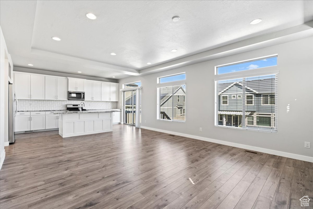 Unfurnished living room featuring baseboards, a tray ceiling, recessed lighting, and wood finished floors