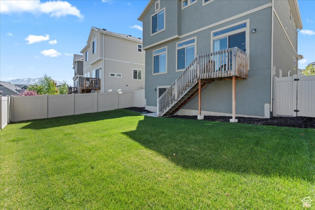 Back of house with a fenced backyard, stucco siding, a lawn, and stairway