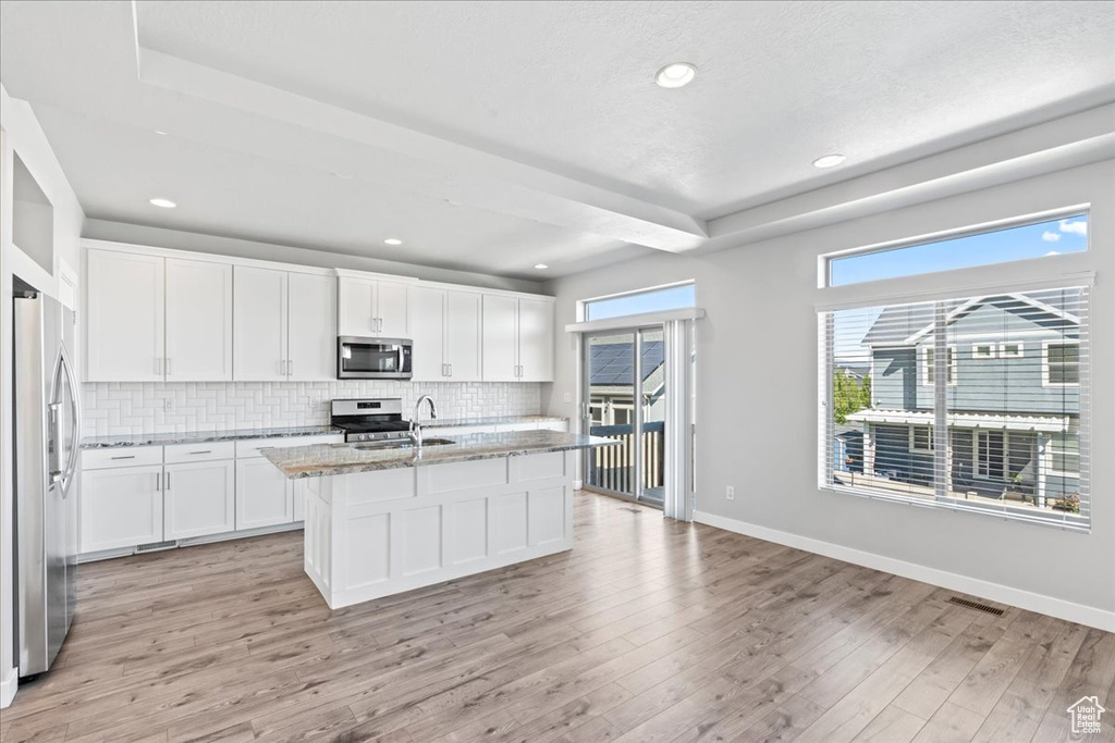 Kitchen featuring appliances with stainless steel finishes, tasteful backsplash, light stone countertops, baseboards, and light wood finished floors