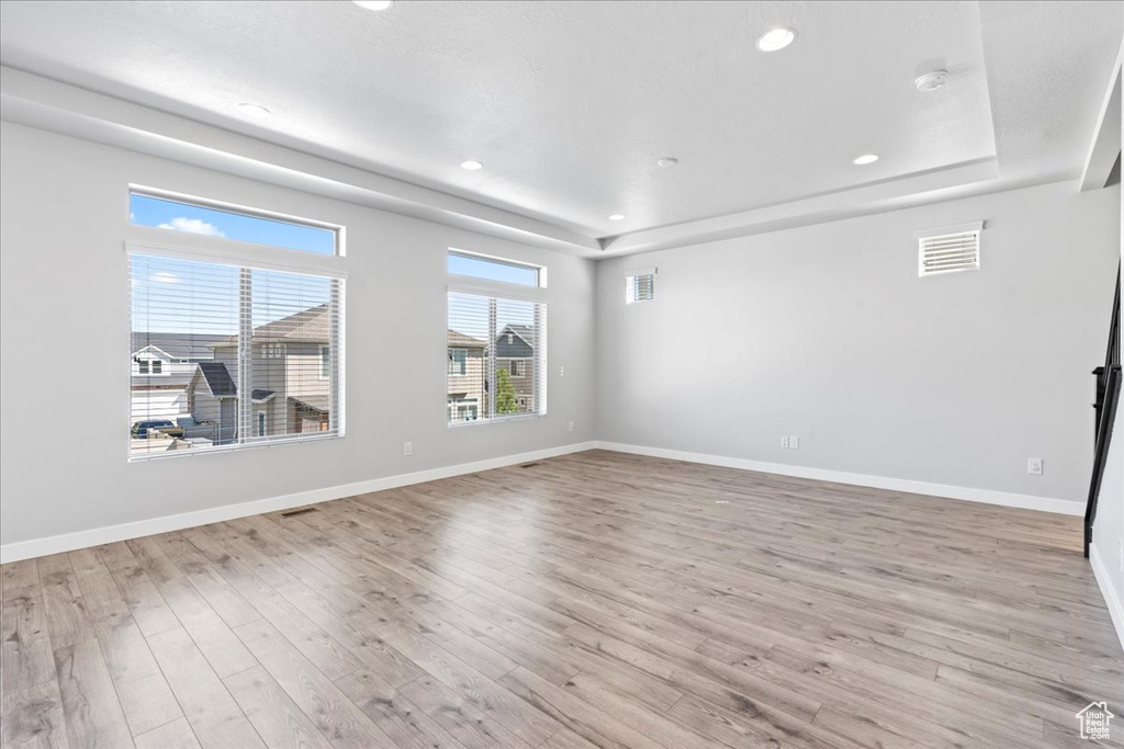 Unfurnished living room with visible vents, light wood finished floors, and a tray ceiling