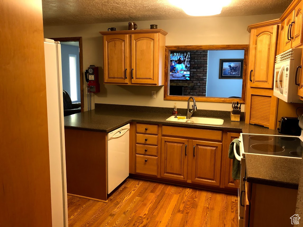 Kitchen with a textured ceiling, dark countertops, wood finished floors, a sink, and white appliances