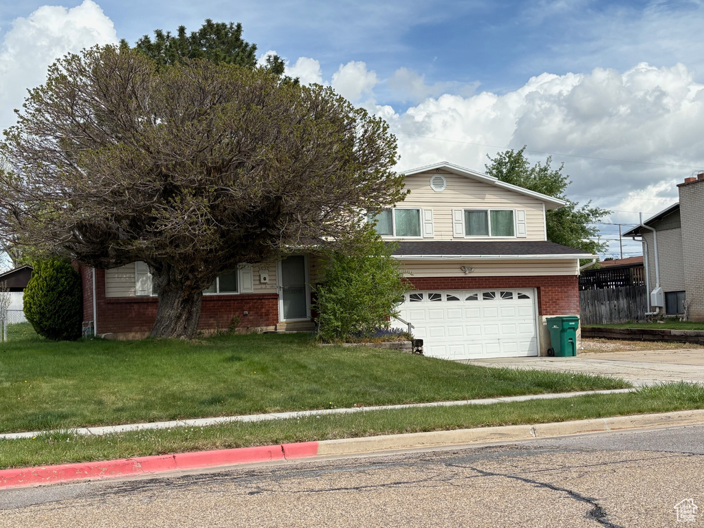 View of front of property featuring concrete driveway, brick siding, a front yard, and a garage
