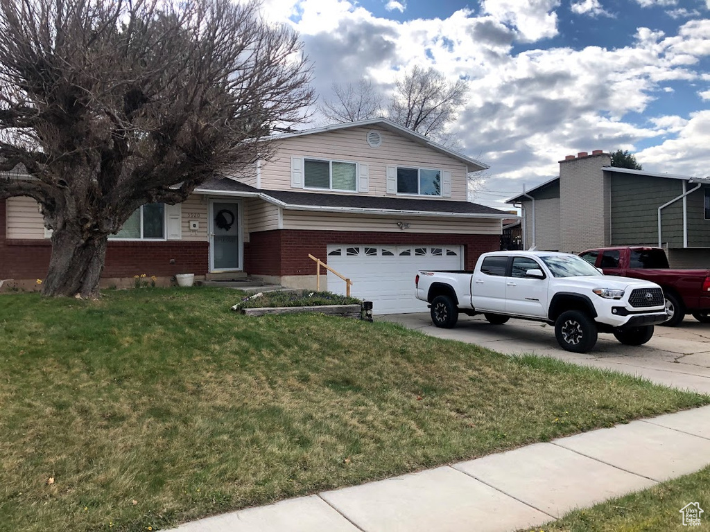 Split level home with brick siding, a front lawn, an attached garage, and driveway