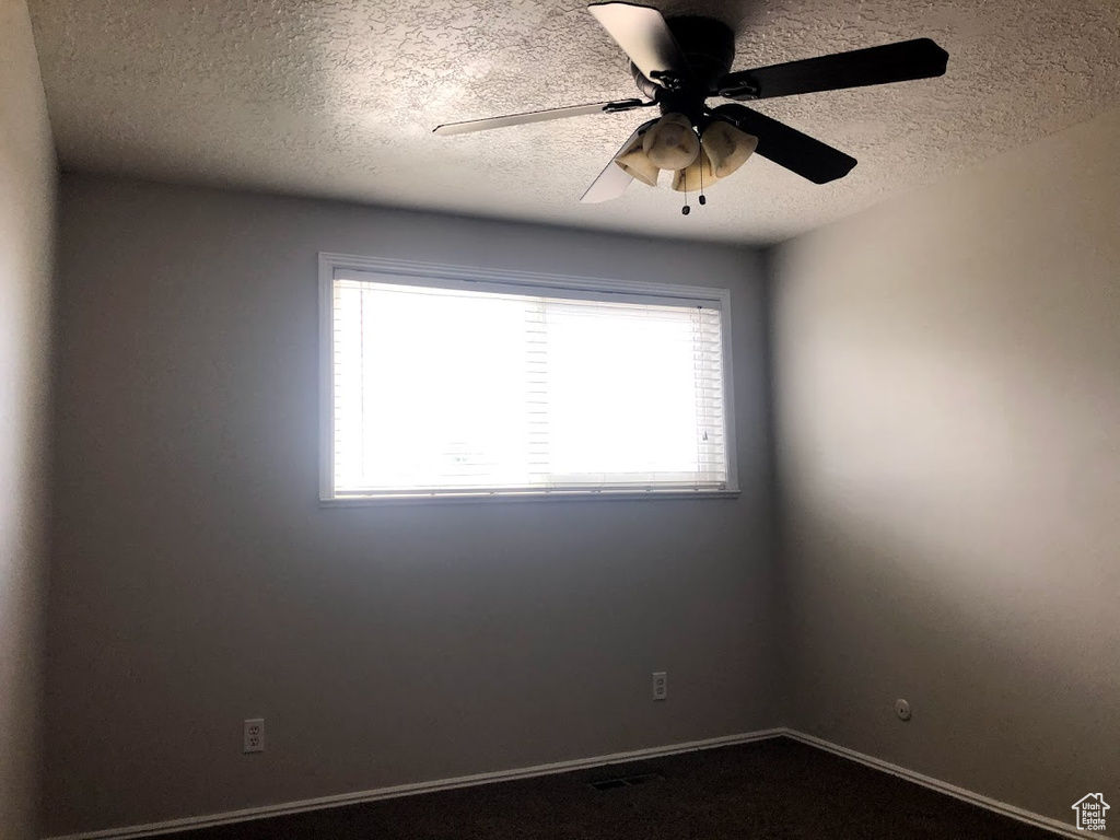 Empty room featuring dark carpet, a textured ceiling, ceiling fan, and baseboards