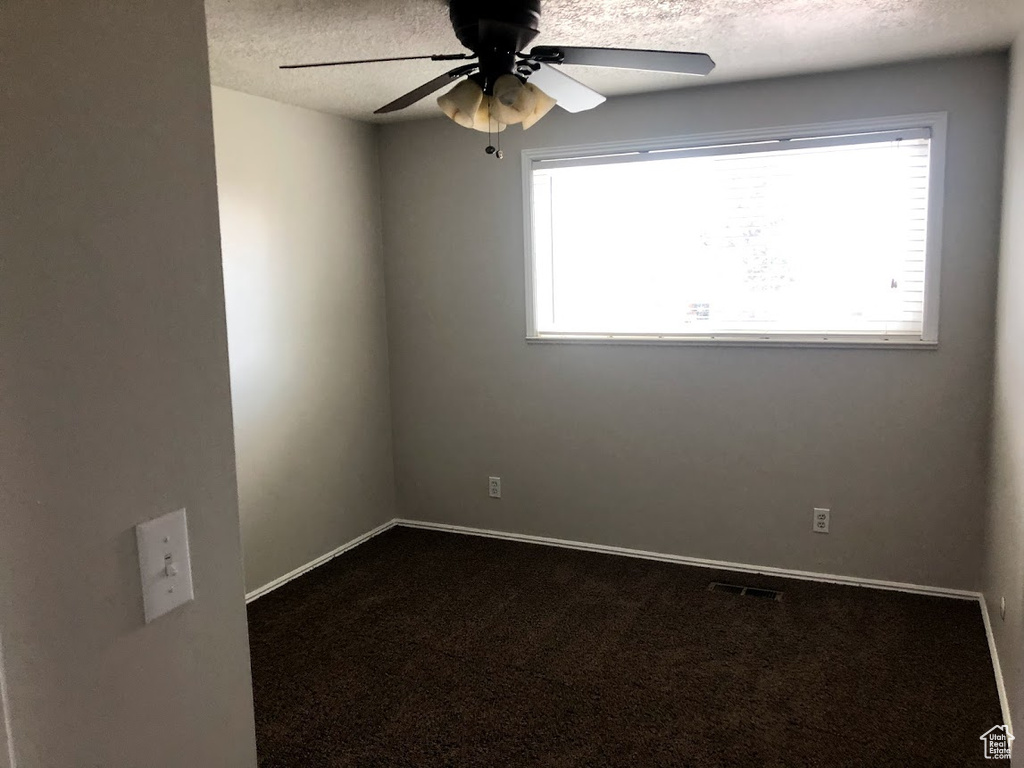 Carpeted empty room with a ceiling fan, a textured ceiling, visible vents, and a healthy amount of sunlight