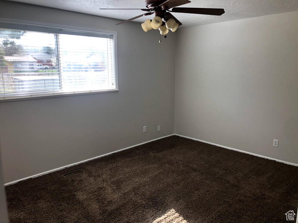 Spare room with dark colored carpet, a textured ceiling, and ceiling fan
