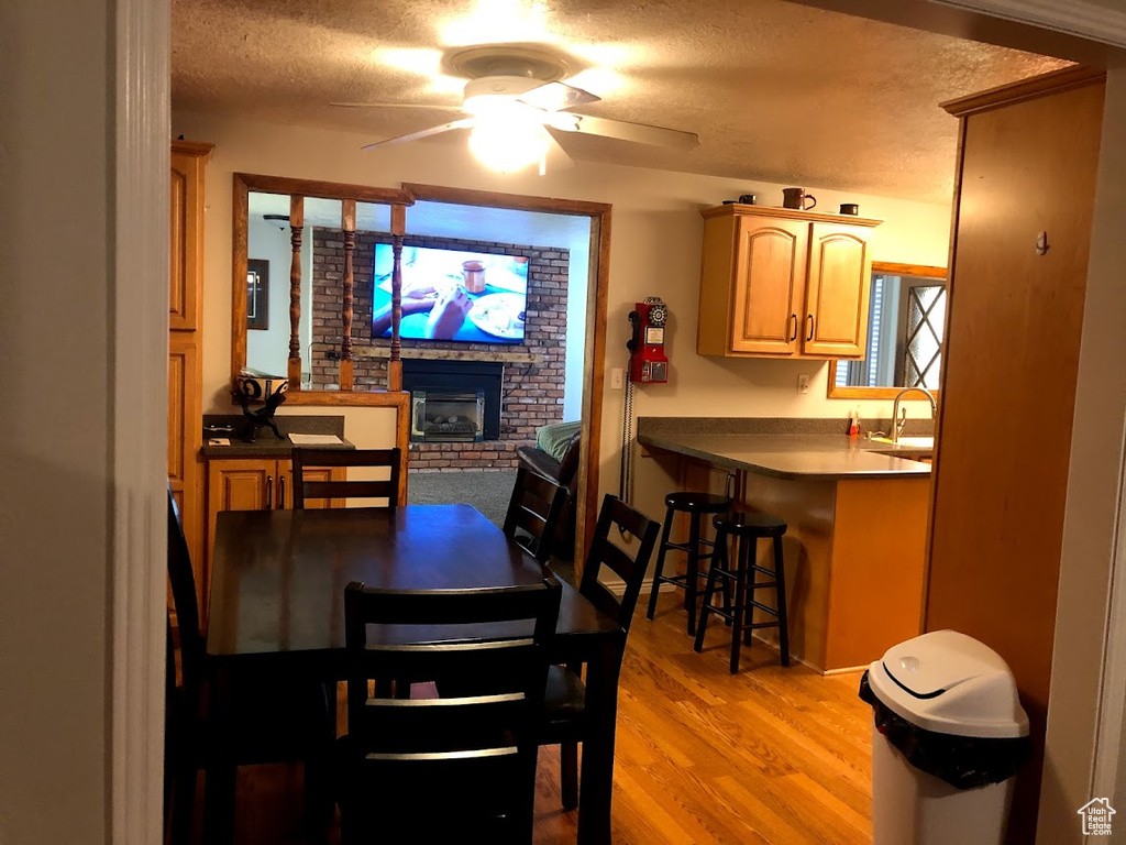 Dining space featuring a ceiling fan, a textured ceiling, a brick fireplace, and light wood-style flooring