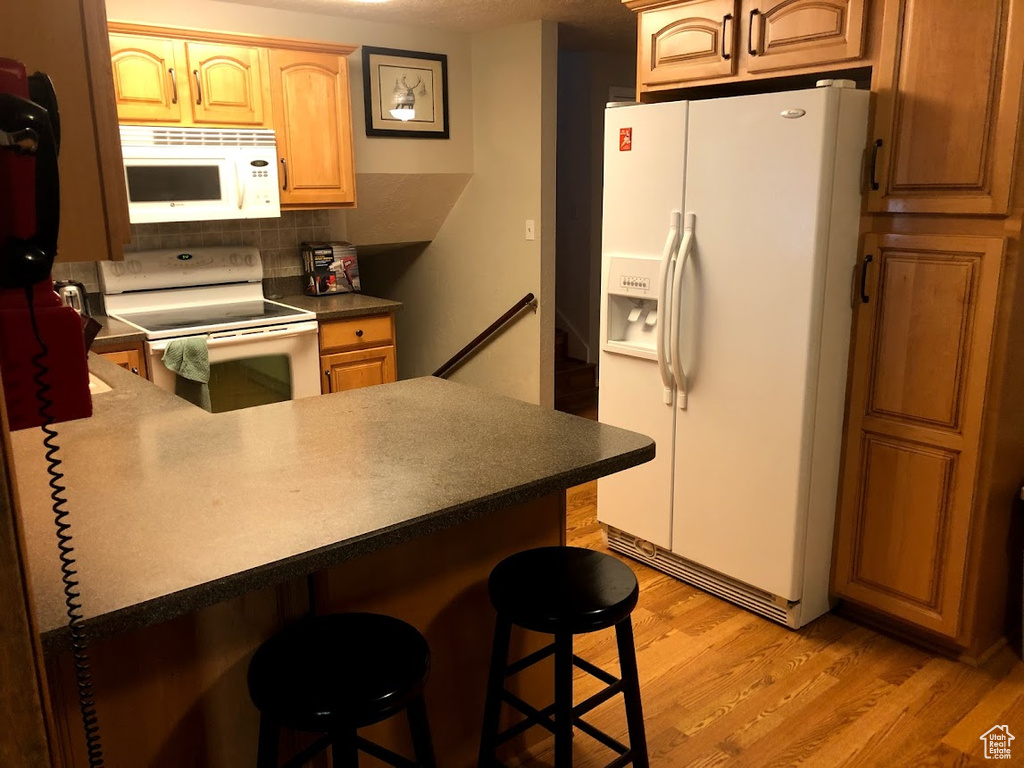 Kitchen with a kitchen breakfast bar, tasteful backsplash, light wood-type flooring, a peninsula, and white appliances