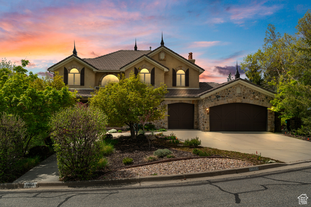 French country style house with stucco siding, driveway, a tile roof, and stone siding