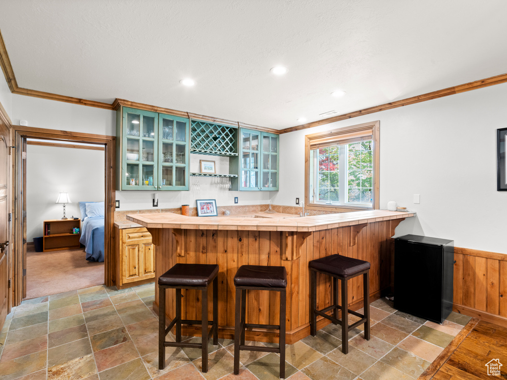 Kitchen featuring a kitchen breakfast bar, refrigerator, stone finish flooring, and ornamental molding