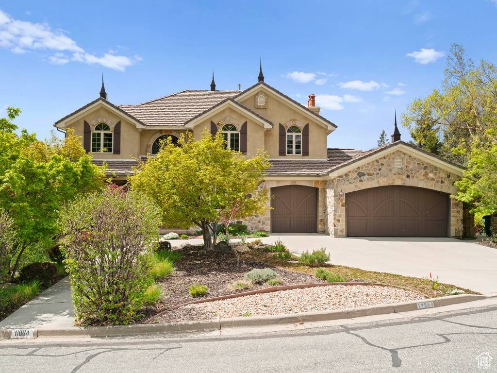 View of front of home with stone siding, a garage, stucco siding, a chimney, and concrete driveway
