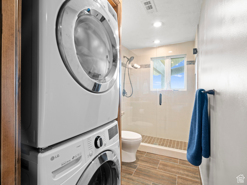 Clothes washing area featuring laundry area, wood finish floors, stacked washing maching and dryer, recessed lighting, and visible vents