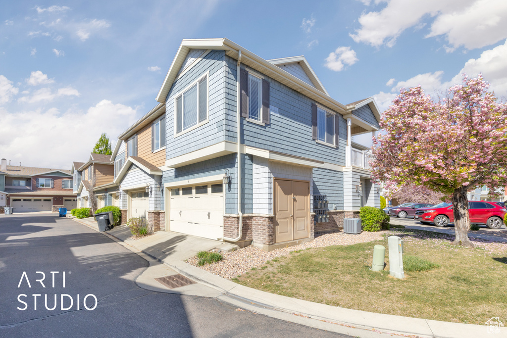 Townhome / multi-family property with a residential view, an attached garage, central AC, brick siding, and a front yard