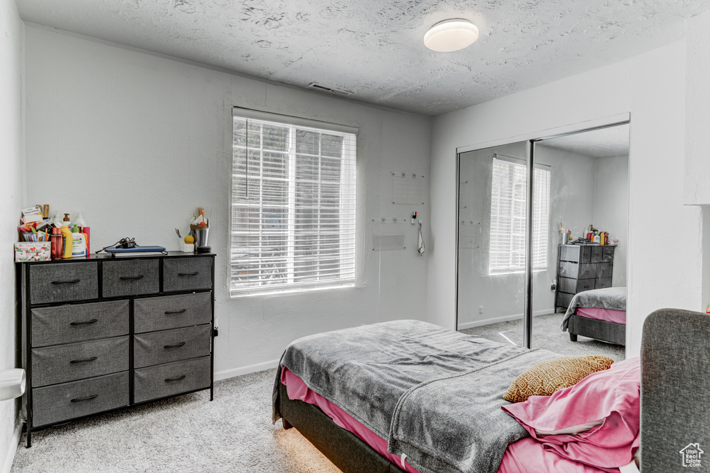 Bedroom featuring visible vents, a closet, baseboards, light colored carpet, and a textured ceiling