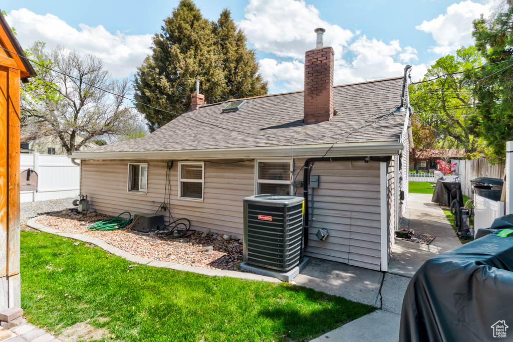 Exterior space with central AC, fence, roof with shingles, a chimney, and a lawn