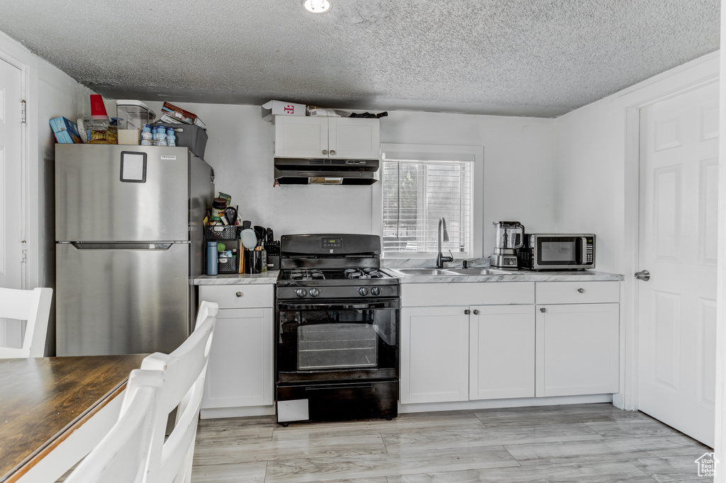 Kitchen with a textured ceiling, a sink, under cabinet range hood, stainless steel appliances, and white cabinetry