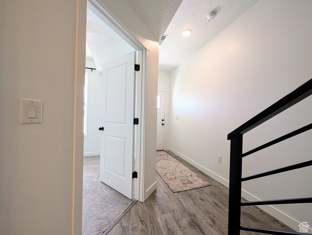 Hall featuring baseboards, a textured ceiling, wood finished floors, and visible vents