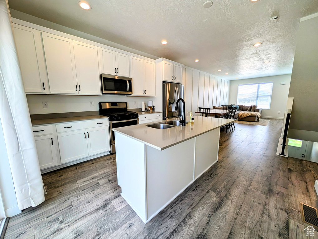 Kitchen featuring a sink, appliances with stainless steel finishes, a center island with sink, and wood finished floors