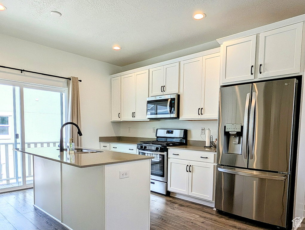 Kitchen with appliances with stainless steel finishes, a sink, a center island with sink, white cabinetry, and dark wood-style floors