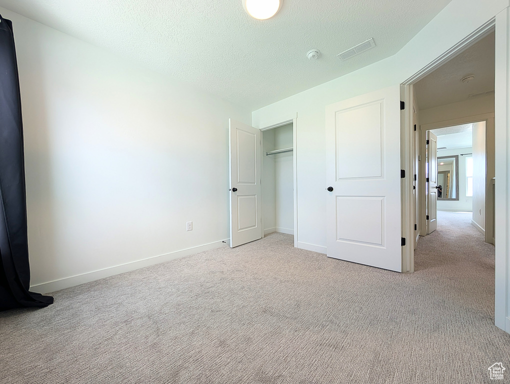 Unfurnished bedroom featuring a textured ceiling, visible vents, baseboards, a closet, and light carpet