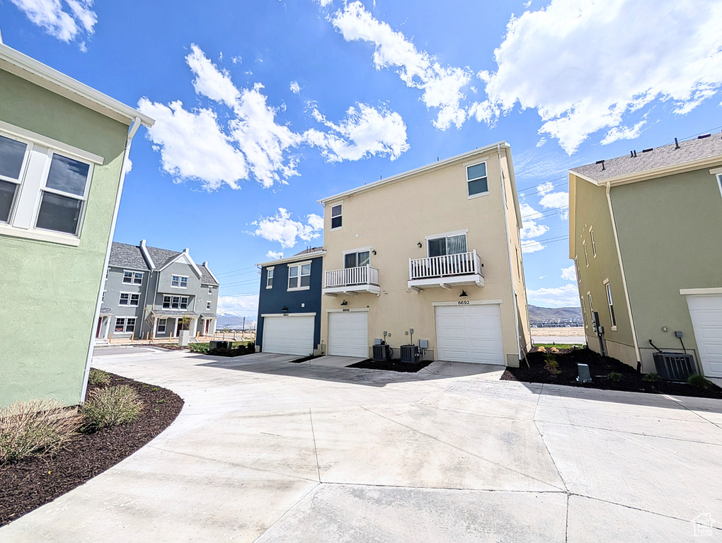 Back of property featuring a garage, central AC, stucco siding, concrete driveway, and a residential view