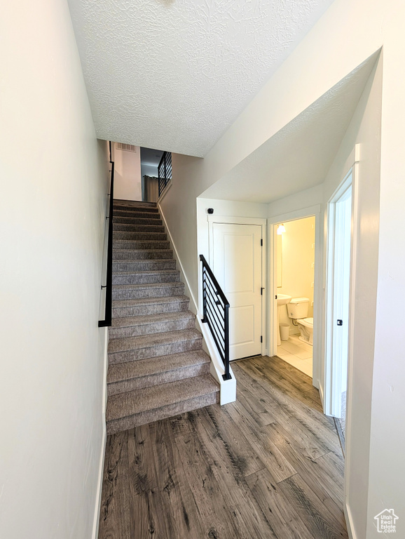 Staircase featuring a textured ceiling, baseboards, and wood finished floors
