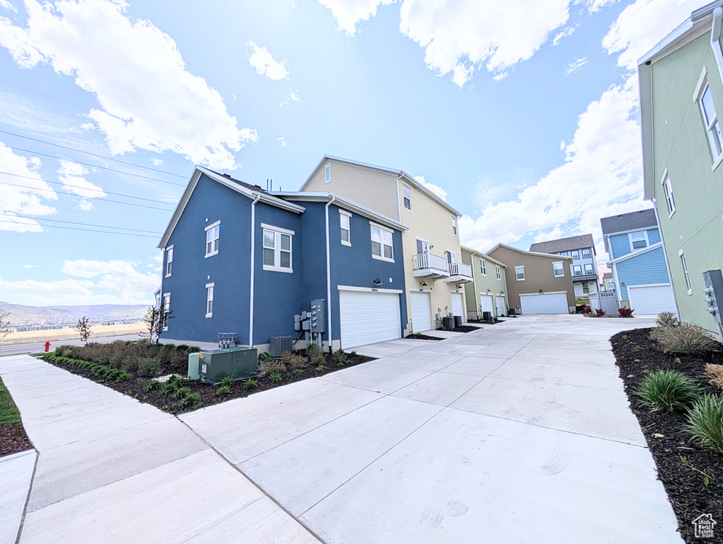 View of side of home with stucco siding, central AC unit, an attached garage, driveway, and a residential view