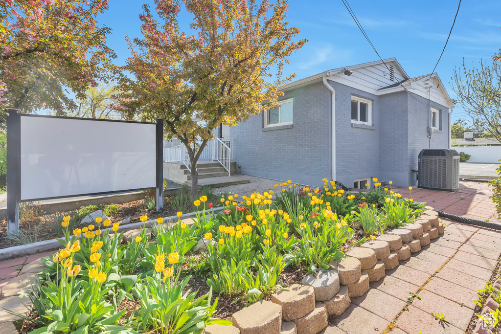 View of side of property featuring brick siding, central AC unit, and a patio area