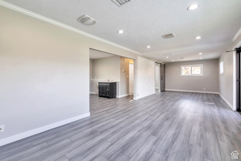 Unfurnished living room featuring a barn door, recessed lighting, baseboards, wood finished floors, and ornamental molding