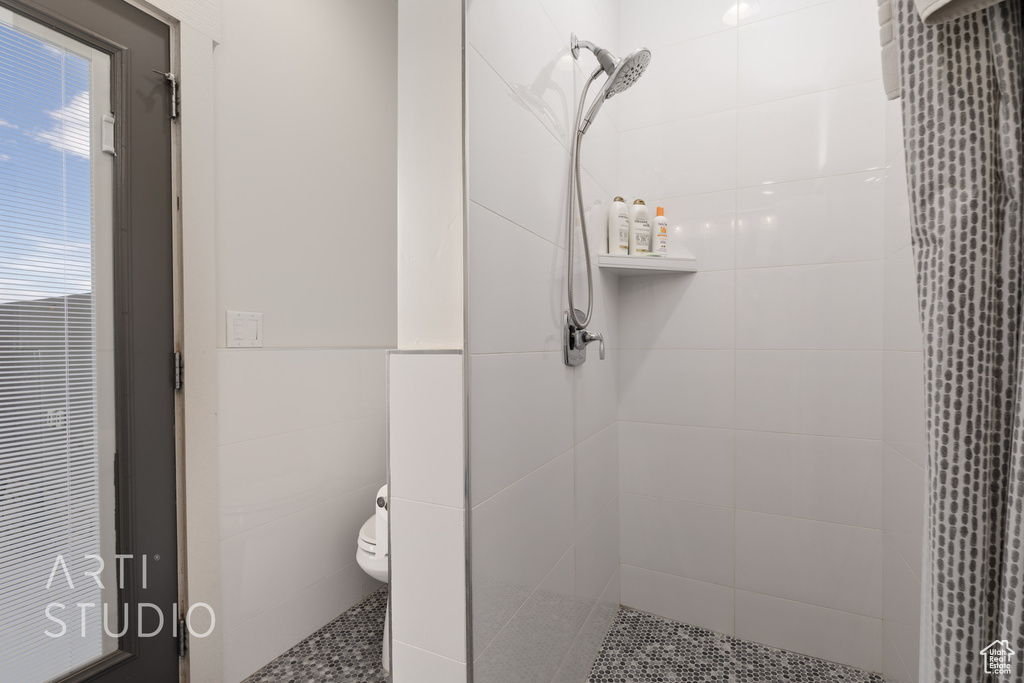 Bathroom with a tile shower, toilet, and tile walls