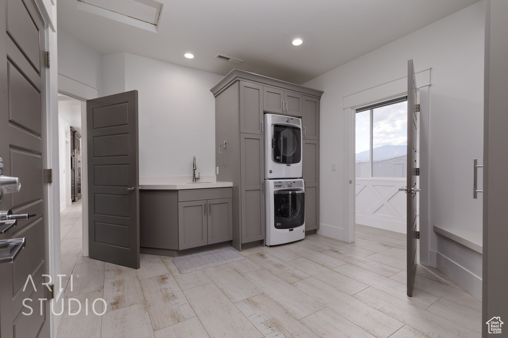 Kitchen with stacked washer and dryer, a sink, gray cabinets, light wood-style flooring, and visible vents