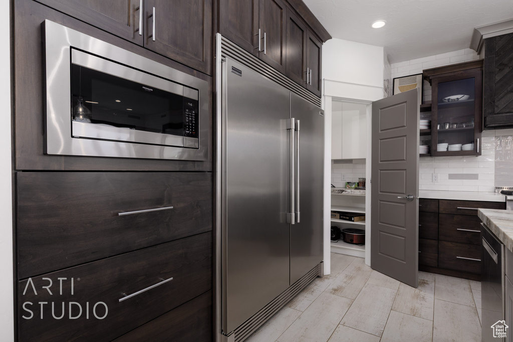Kitchen with light countertops, built in appliances, tasteful backsplash, and dark brown cabinetry