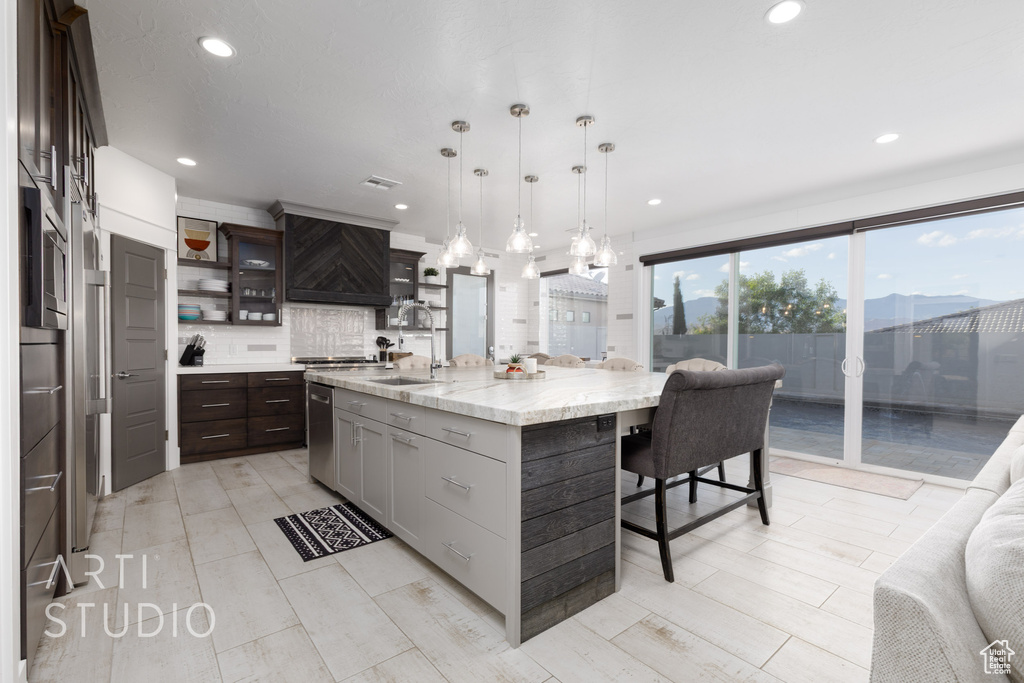 Kitchen with a breakfast bar, a sink, recessed lighting, decorative backsplash, and custom exhaust hood