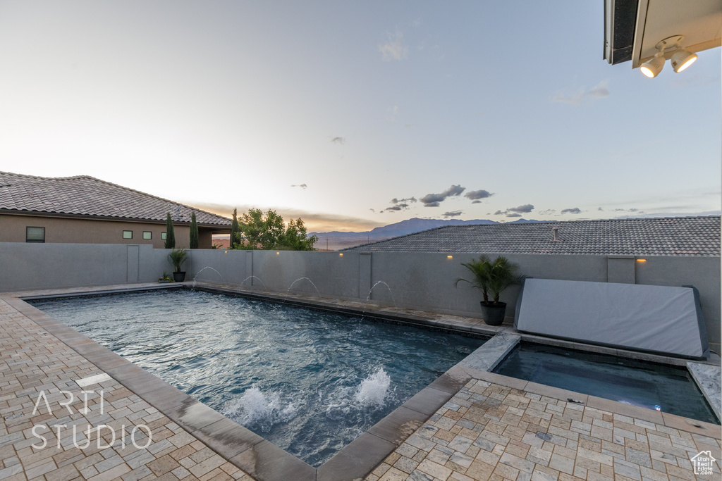 Pool at dusk with a fenced in pool, a fenced backyard, an in ground hot tub, and a patio area