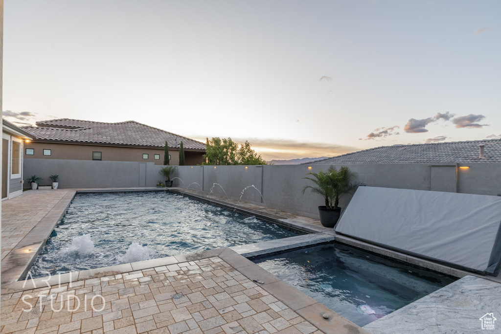 Pool at dusk featuring a fenced in pool, a fenced backyard, an in ground hot tub, and a patio